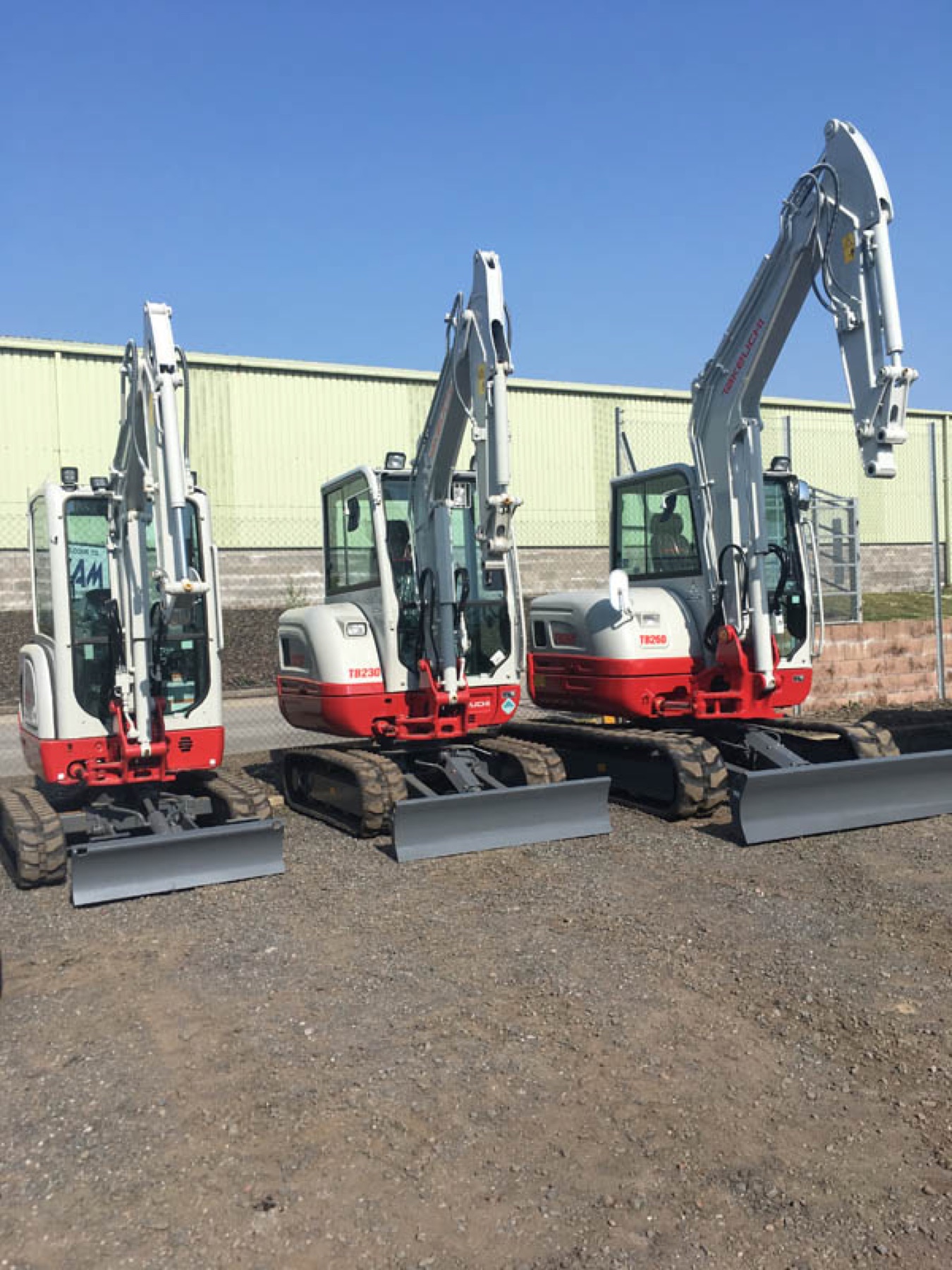 Three Takeuchi diggers lined up in a row in the yard.