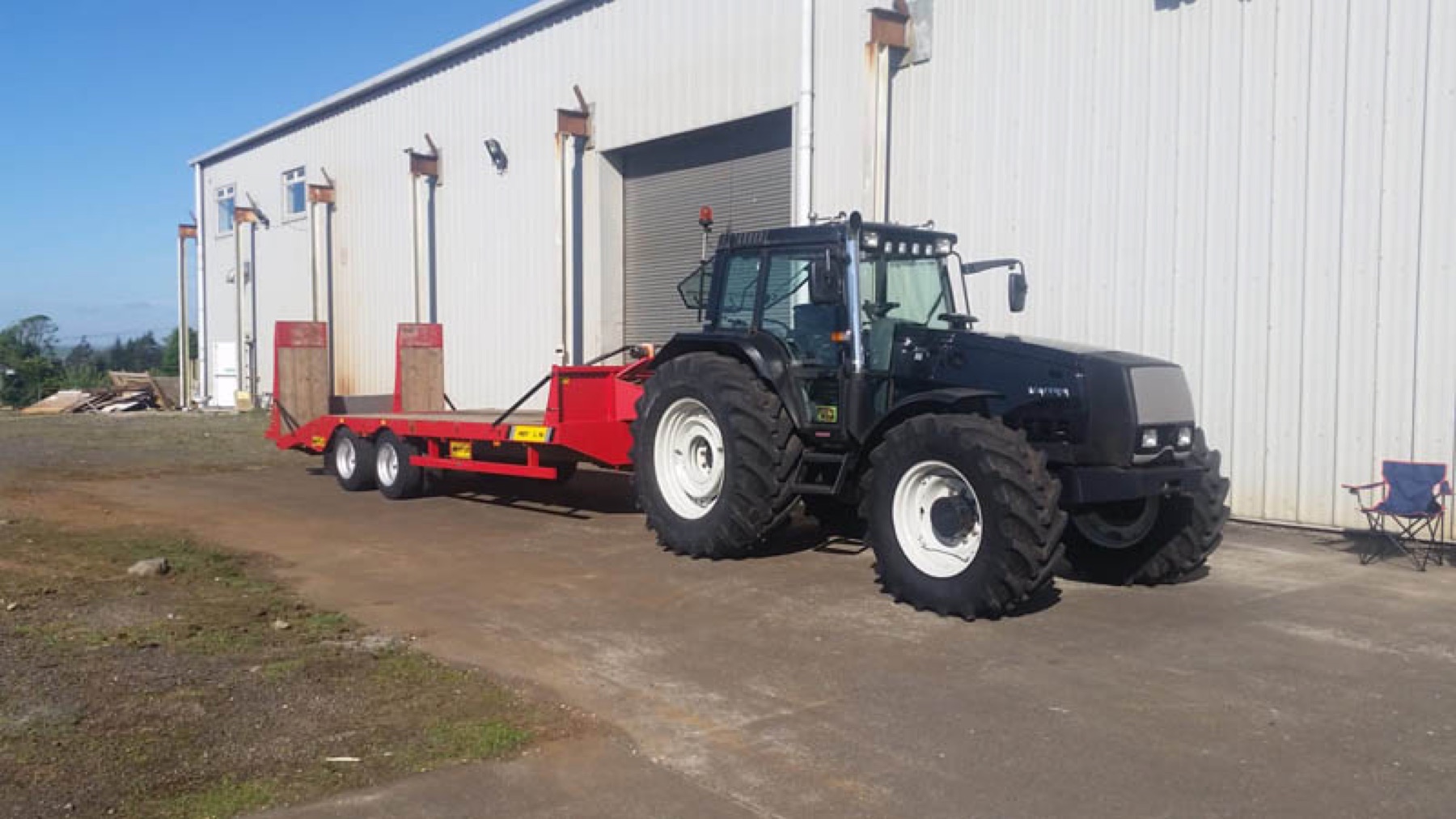 A Valtra tractor with a trailer in the yard.